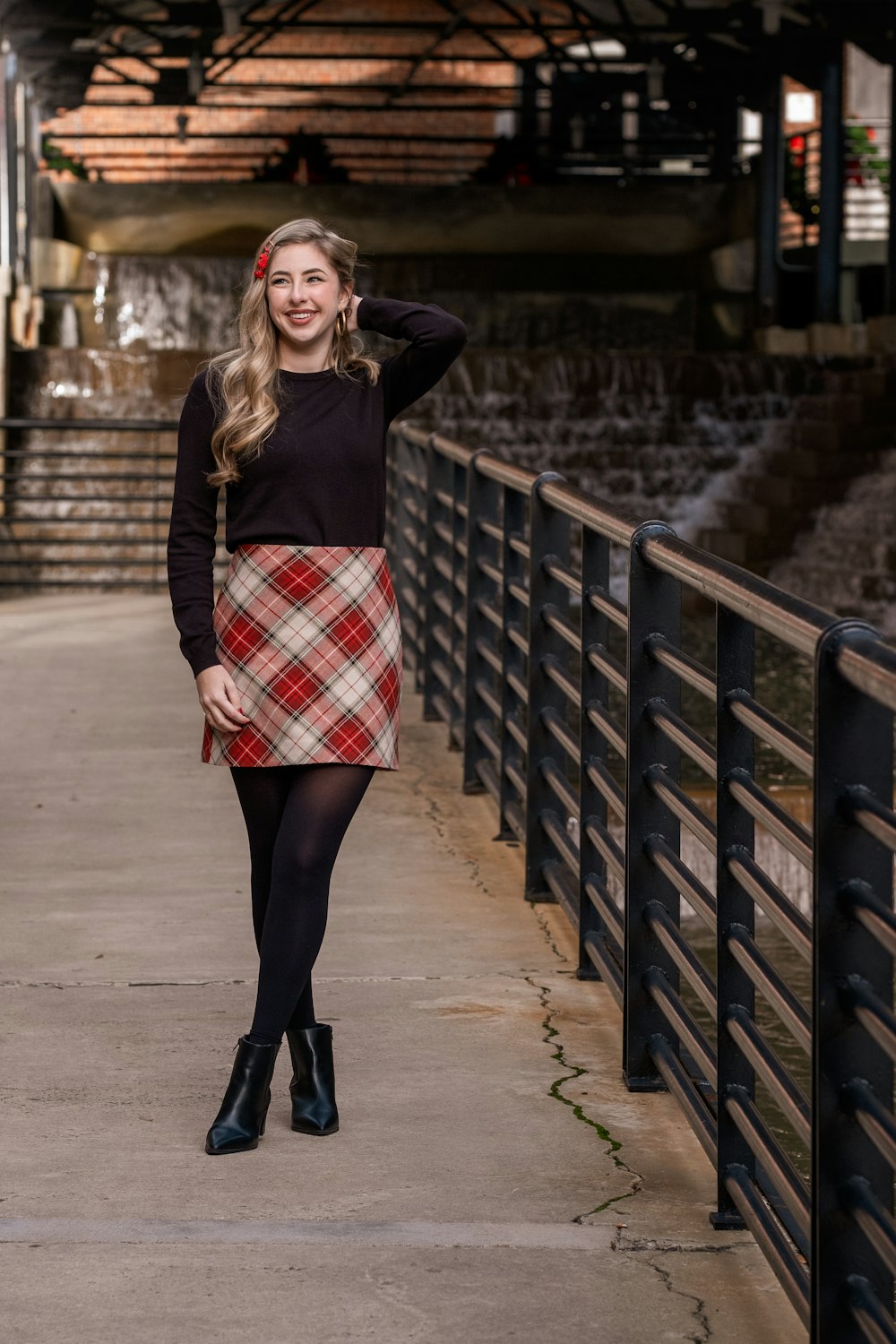 woman in black long sleeve shirt and red white plaid mini skirt standing on brown concrete