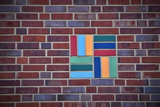 A brick wall with a patterned section of colored rectangular tiles. The tiles include shades of blue, green, orange, and red arranged in a geometric pattern.
