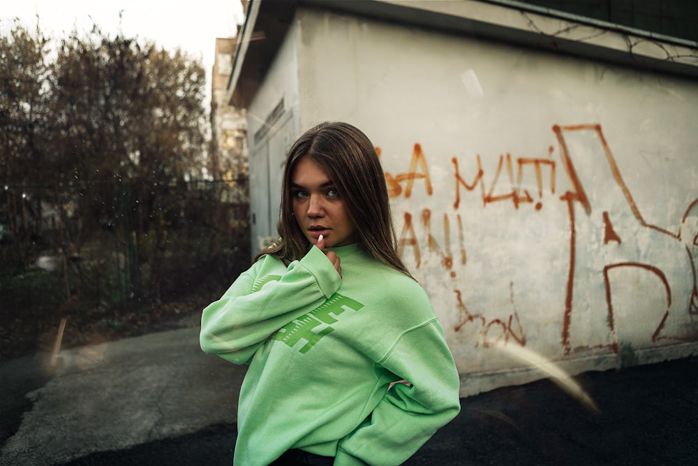 woman in green hoodie standing beside white wall during daytime