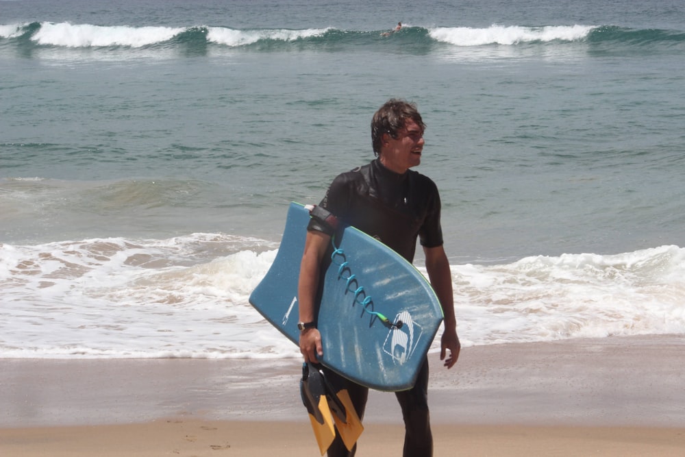 man in black shirt holding blue surfboard on beach during daytime