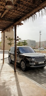 A Range Rover parked on a gravel path winding through rolling green fields under a cloudy sky.