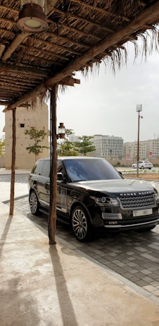 A Range Rover parked on a gravel path winding through rolling green fields under a cloudy sky.