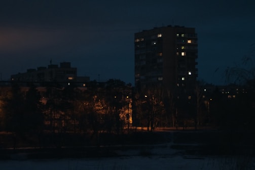 Nighttime photo of a completed mixed-use building illuminated with warm lighting.