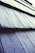 Close-up view of textured roof shingles covered in frost or ice, with a diagonal perspective that draws the eye across the pattern. The surface appears rough, with a light dusting of frost giving a sparkling effect under the light.