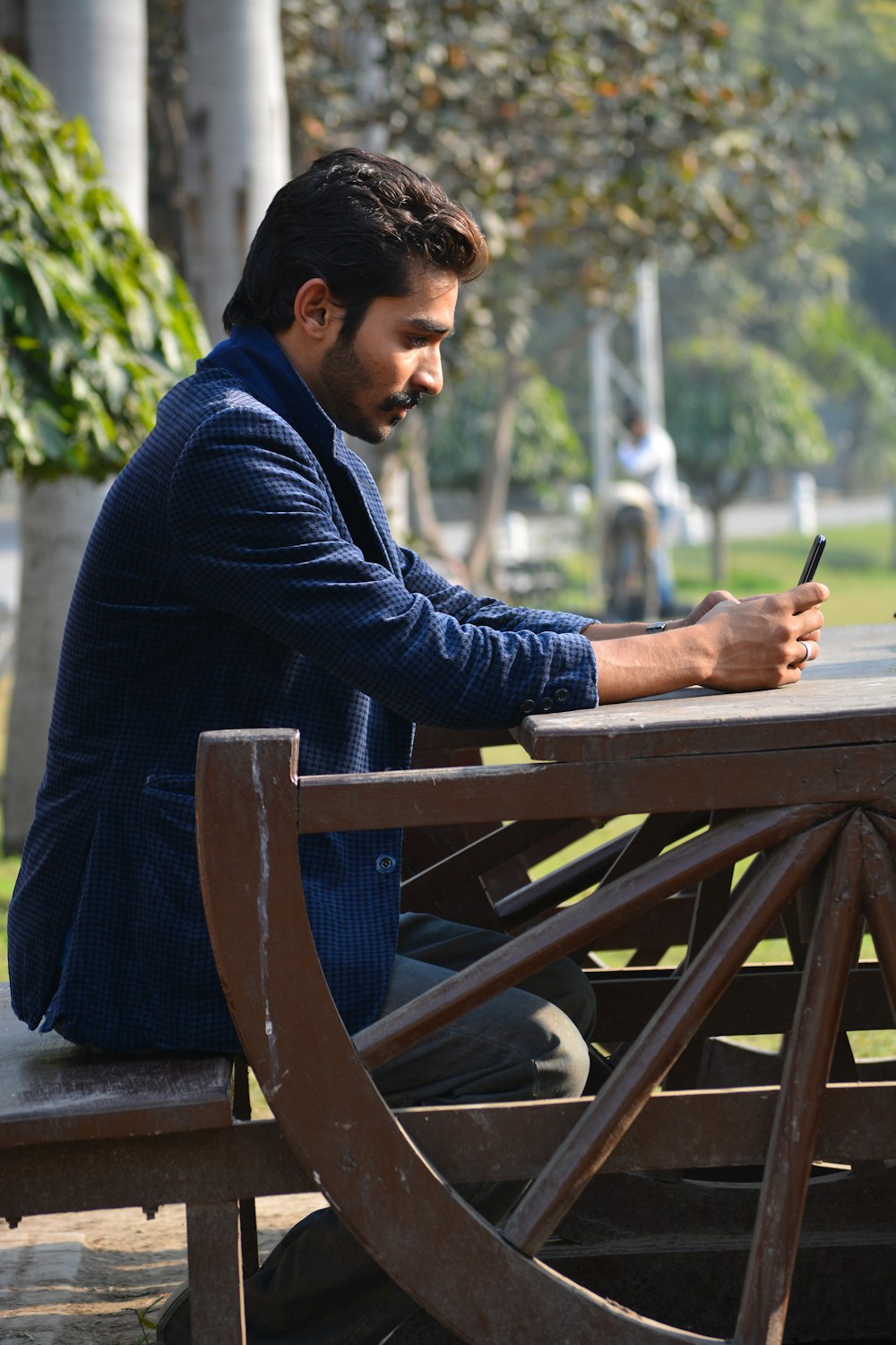 man in blue sweater and blue denim jeans sitting on brown wooden bench during daytime