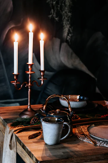A cozy dining table set with warm earthenware, cardamom pods, and flickering candles, inviting guests to an intimate meal.