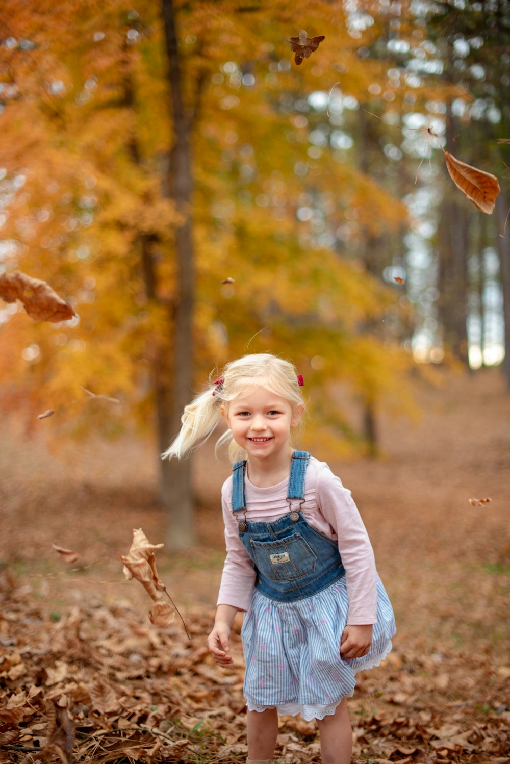 girl in blue denim vest and blue denim dungaree standing on brown grass field during daytime