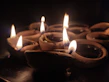 Array of brass and copper diyas glowing softly on a deep red cloth backdrop.