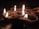 A cluster of small clay lamps, traditionally known as diyas, are lit and arranged on a dark surface. The warm glow of the flames creates a soft, serene atmosphere. The background is dimly lit, highlighting the gentle flicker of the fire against the clay texture.