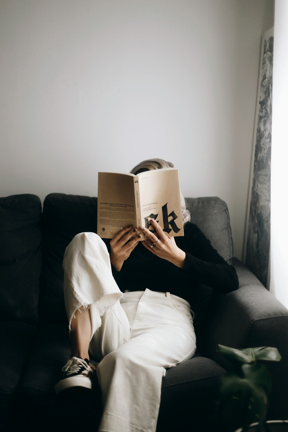 Mujer en camisa blanca leyendo libro sentado en sofá negro
