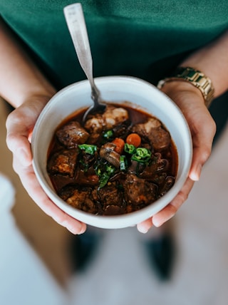 person holding white ceramic bowl with soup