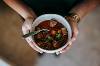 Hands holding a jar of risotto with a spoon ready to enjoy, against a warm background.