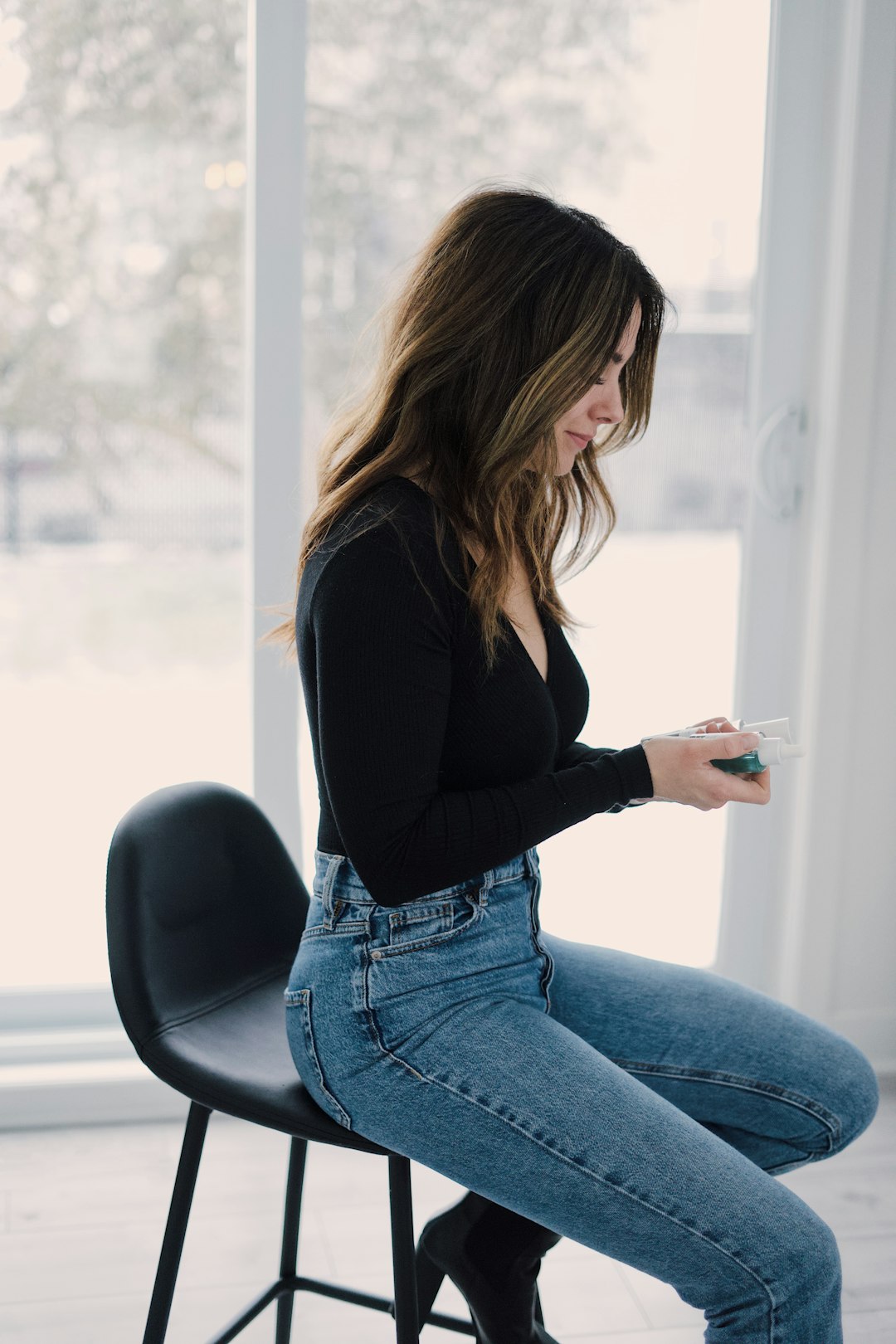 woman in black long sleeve shirt and blue denim jeans sitting on black chair