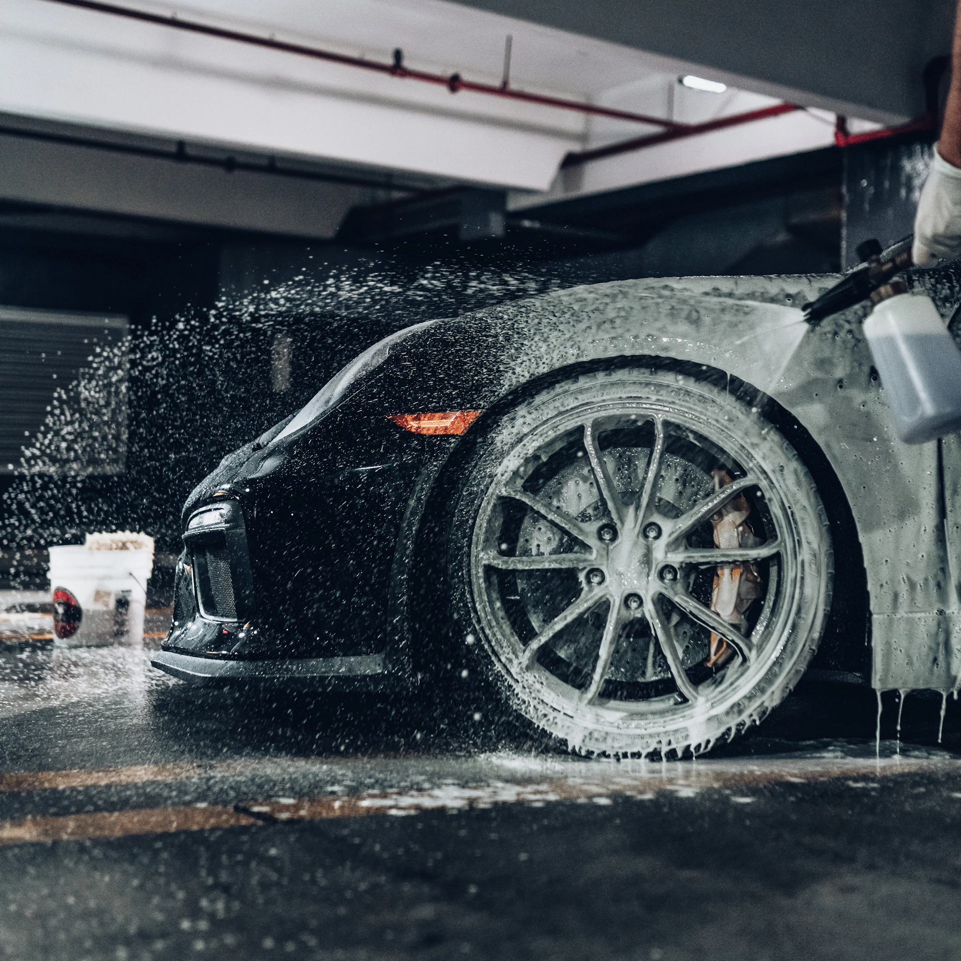 Thick foam being sprayed onto a dark sports car during a hand wash