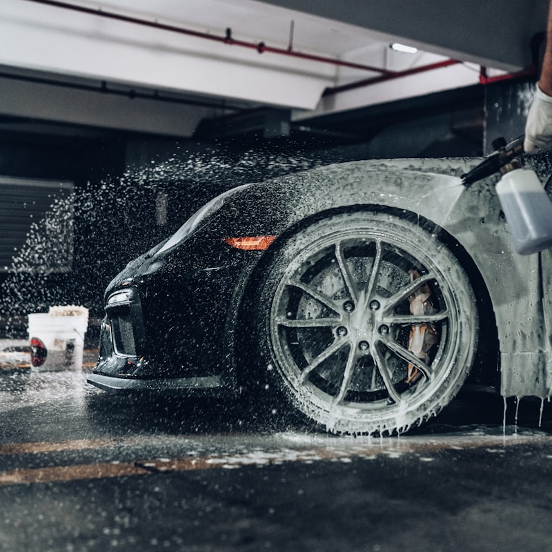 Professional detailer washing a vehicle with microfiber mitt and foam