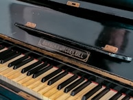 A close-up view of a piano keyboard with visible brand name 'Burger & Jacoby, Biel.' The keys are slightly aged with some wear, showing black and white keys typical of a traditional piano. The piano's surface appears polished but shows signs of use with small hinges attached.