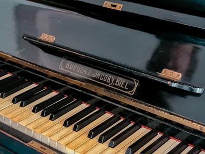 A close-up view of a piano keyboard with visible brand name 'Burger & Jacoby, Biel.' The keys are slightly aged with some wear, showing black and white keys typical of a traditional piano. The piano's surface appears polished but shows signs of use with small hinges attached.