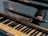 A close-up view of a piano keyboard with visible brand name 'Burger & Jacoby, Biel.' The keys are slightly aged with some wear, showing black and white keys typical of a traditional piano. The piano's surface appears polished but shows signs of use with small hinges attached.