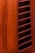 A close-up view of a bright orange surface with parallel rectangular ventilation slits. The surface has a glossy finish with some visible imperfections or speckles.