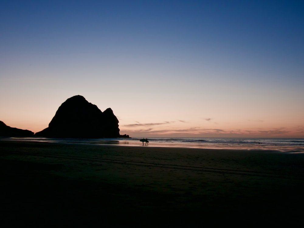 silhouette of rock formation on sea during sunset