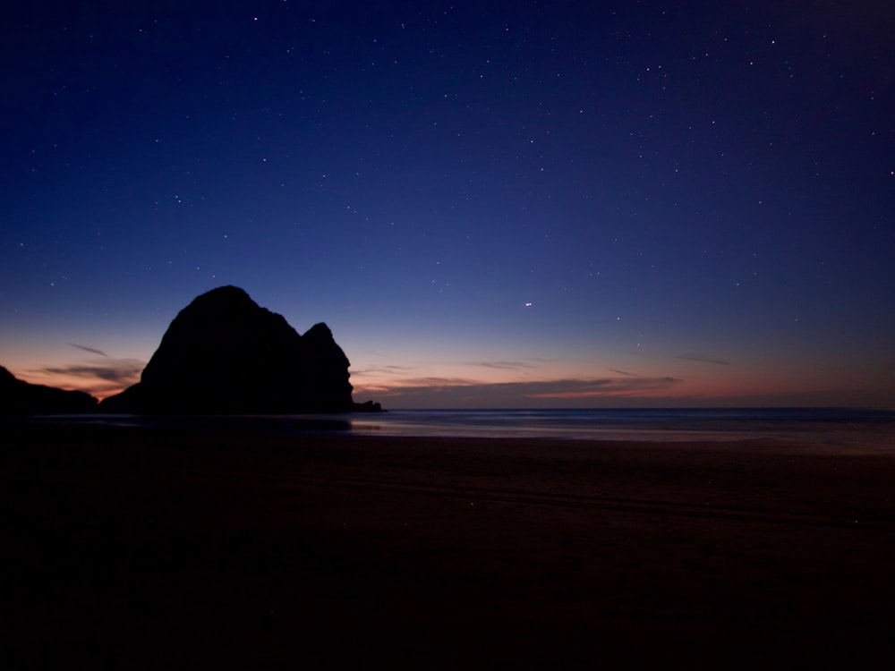 silhouette of rock formation on sea shore during night time