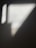 A shadow is cast on a textured surface, forming geometric shapes with varied shades of gray. The lighting creates a contrast against the backdrop, highlighting the wall's subtle imperfections and giving it depth.