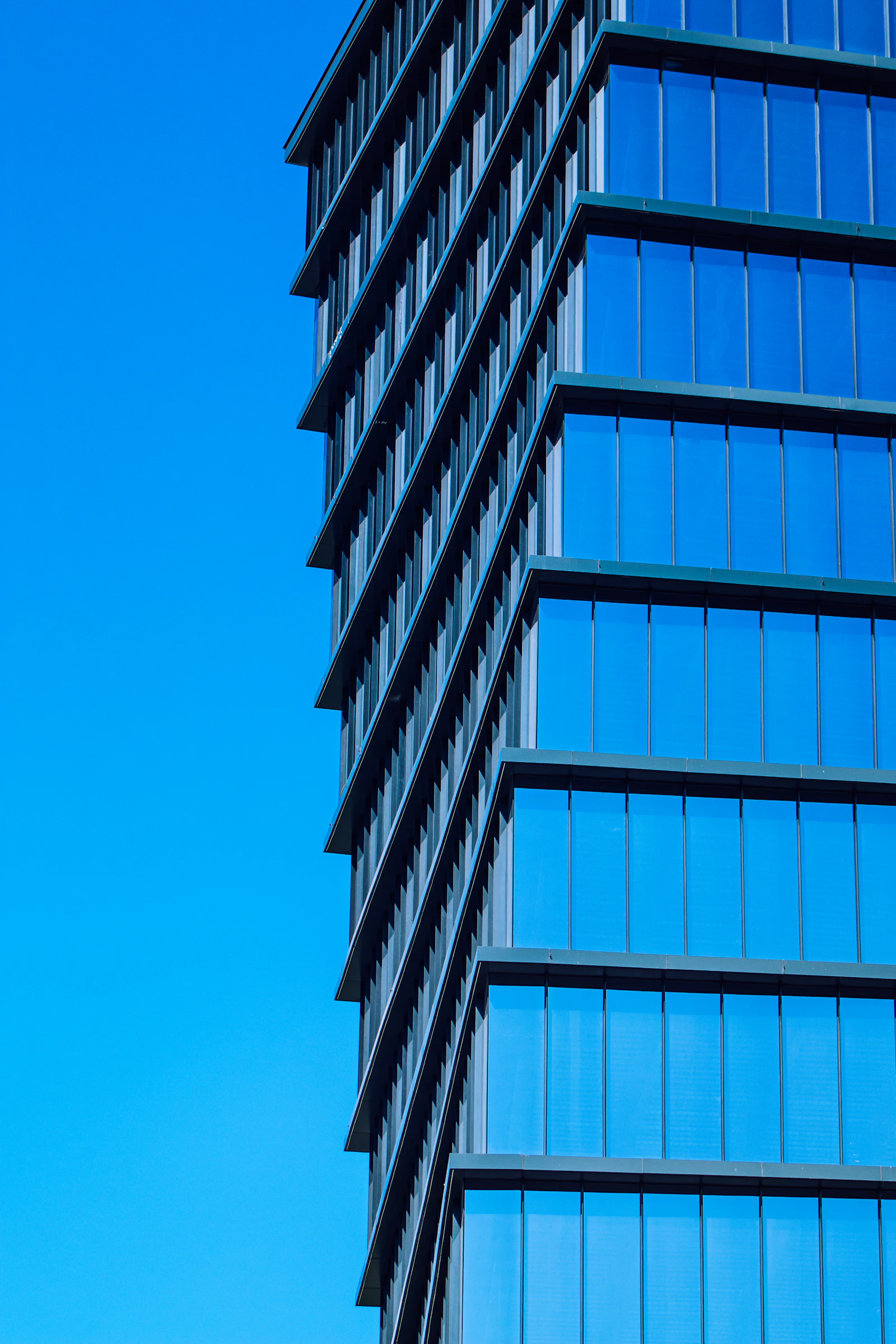 A glass curtain wall tower against open sky, seen from below