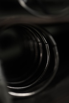 A close-up view of a series of circular metallic rings or coils, aligned in a tunnel-like formation. The image is dark, with subtle reflections of light on the metallic surfaces, creating a sense of depth and mystery.