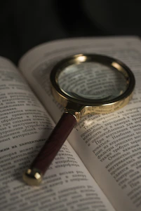 A close-up of a vintage-style magnifying glass resting on an open book, sunlight highlighting the glass.