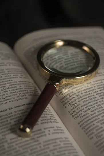 A close-up of a vintage-style magnifying glass resting on an open book, sunlight highlighting the glass.