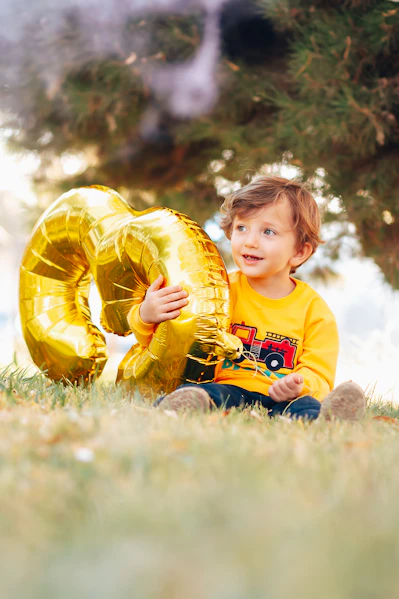 boy in yellow and white crew neck t-shirt holding yellow inflatable balloon on green grass