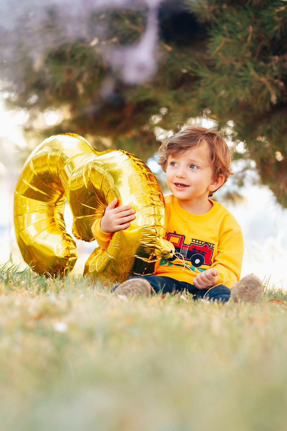 boy in yellow and white crew neck t-shirt holding yellow inflatable balloon on green grass