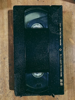 A faded VHS tape labeled 'Madison 1995 Live Session' resting on a wooden table covered with scattered concert tickets and handwritten setlists.