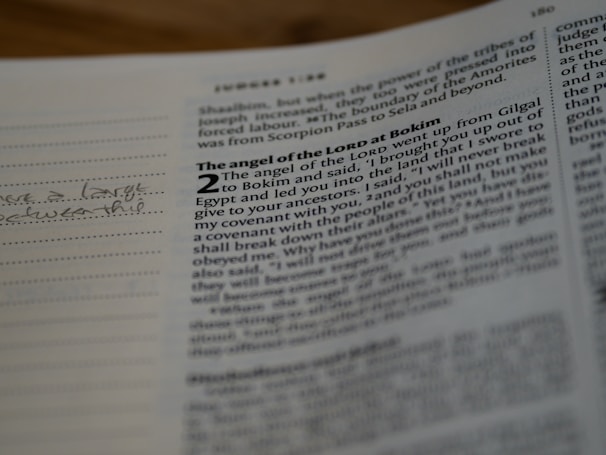 A close-up of an open book with printed text. The page is formatted with two columns; on the left, there is a handwritten note in cursive on lined space, and on the right, there is a passage with bolded titles and numerical markings.