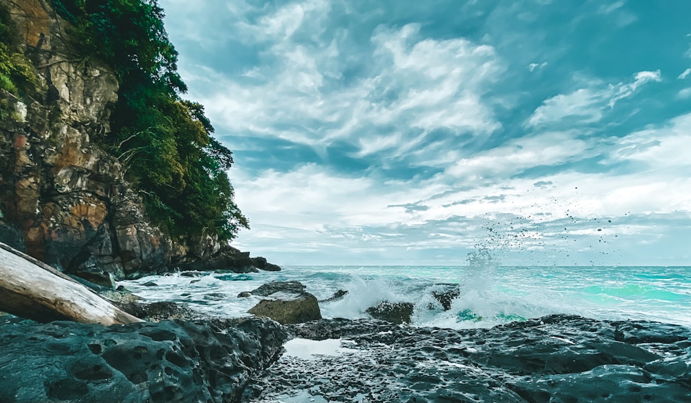 ocean waves crashing on rocks under white clouds and blue sky during daytime