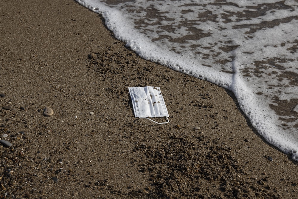 Tabla de madera blanca y marrón sobre arena marrón cerca del cuerpo de agua durante el día