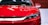A sleek, modern car with a shiny red finish and sharp headlights. The front grille features a distinctive design with chrome accents.