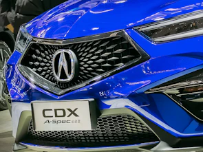 A close-up of a shiny blue car's front grille with yellow lighting reflections.