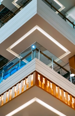 Detailed view of modern architectural elements featuring multiple floors of a building with stylish glass railings. The design includes distinctive geometric patterns and integrated lighting. The clean lines and contrasting colors add to the contemporary aesthetic.