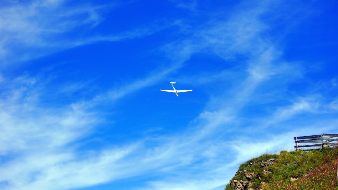 white airplane flying over green grass field under blue sky during daytime