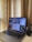 A laptop displaying multiple different applications or windows on its screen is placed on a desk near a set of beige curtains. Next to the laptop on the right is a small black table-top vacuum cleaner.