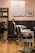 A barbershop interior features vintage-style barber chairs with white and black leather, positioned in front of a wooden floor. The walls are adorned with black-and-white photographs, and a glass panel with the logo and name 'SALA DE BARBA' provides a view into the well-organized space.