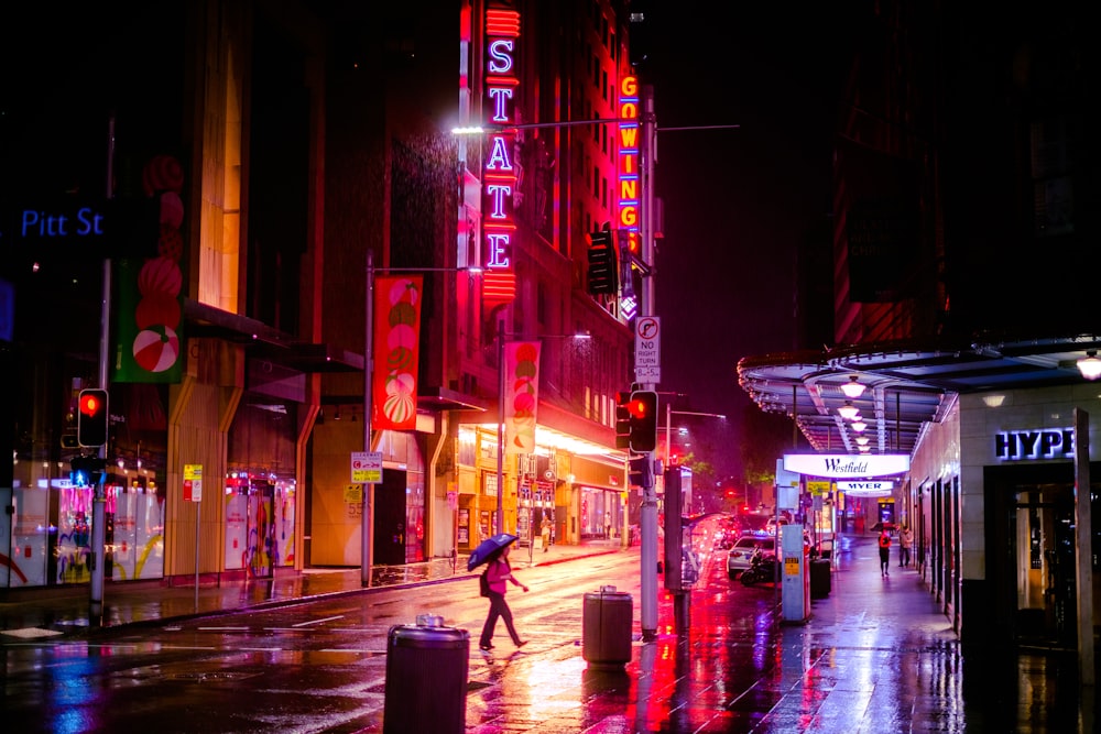 man in black jacket and blue denim jeans walking on street during night time