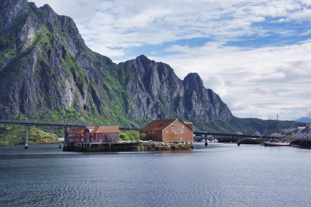 brown wooden house near body of water and mountain under cloudy sky during daytime