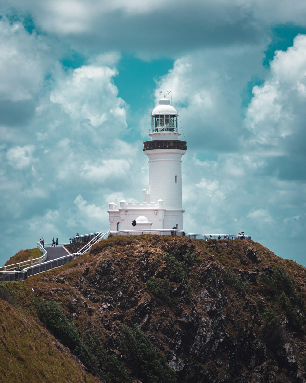 white lighthouse on brown hill under blue sky and white clouds during daytime