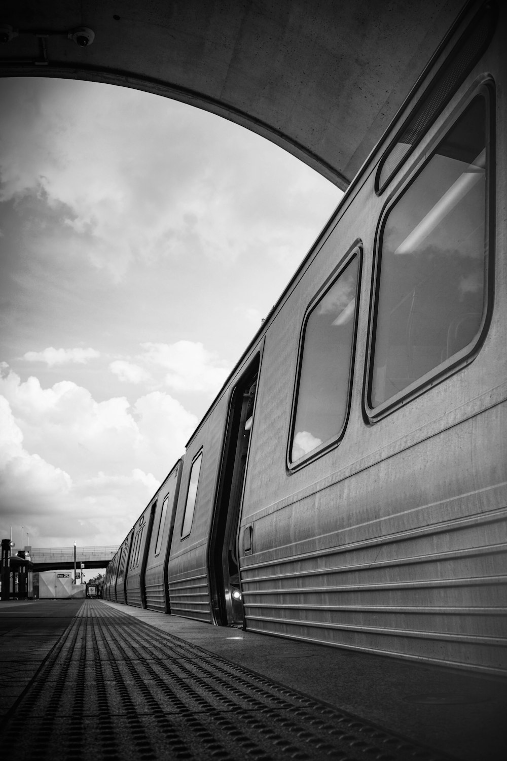 grayscale photo of train under cloudy sky