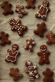 A collection of homemade gingerbread cookies is laid out on a parchment-lined surface. Various shapes are decorated with white icing, including simple smiling gingerbread figures and elaborately designed patterns and swirls.