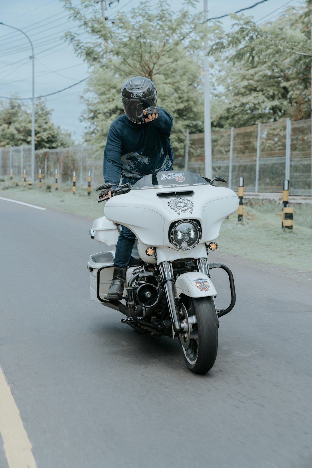 昼間、白いバイクに乗って道路を走る青いジャケットの男