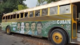 A vintage bus with broken windows and vibrant murals on its side, depicting faces and slogans advocating for peace with Cuba. The artwork includes text such as 'Free the Cuban 5' and a Cuban flag.