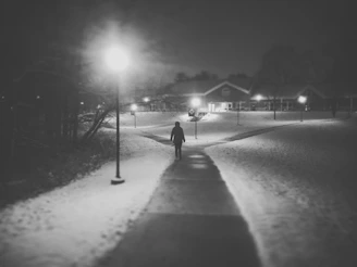 A thoughtful figure walking along a quiet roadside under a starry night sky.